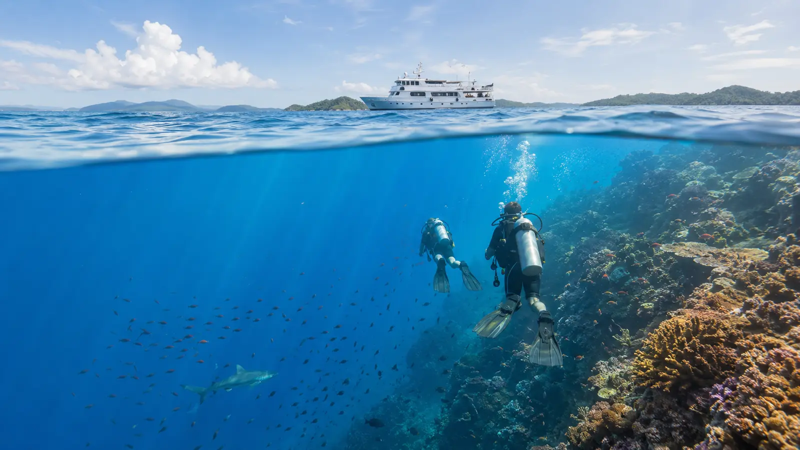 Two scuba divers descending beside a Philippine coral reef with a liveaboard vessel above